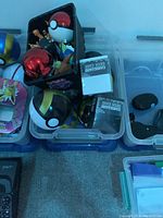 Mix of Pokémon collectible items packed in clear plastic containers including Poké Ball models and card deck cases.