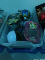 Plastic bin with various Pokémon collectibles including Poké Balls and collectible tins featuring Pokémon characters such as Zapdos.