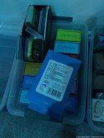 Photo shows a plastic bin containing several pastel-colored Disney 100th anniversary boxes, a black box filled with Pokémon trading cards, small collectible tins, and other containers.