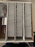 Top-down view of three rows of mixed sports cards in protective sleeves arranged in a white storage box