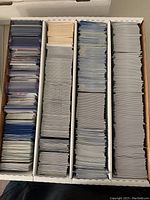 Top view of a multi-compartment white storage box filled with assorted sports cards, many sleeved and sorted in rows.