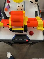 Photo of an orange and yellow Nerf toy blaster laid on a table with sports balls in the background.