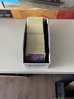 White cardboard box filled with hundreds of Pokémon cards, showing the top view with a Clefable card at the front of the stack.