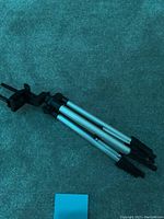 Photo of a compact tripod with silver extendable legs and black feet, featuring a black adjustable smartphone holder mount at the top.