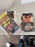 Four VHS tapes placed on a table including a sealed copy of 'Free for All,' 'Audrey Hepburn' documentary, '2001: A Space Odyssey,' and one additional unidentified VHS tape.