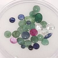 Clear view of loose mixed colored gemstones (sapphire, emerald, ruby, white stones) in round container.