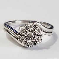 Close-up front view of silver ring showing 7 diamond cluster arranged in floral pattern.