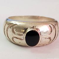 Front view of silver ring with black onyx stone center and engraved pattern on band.