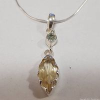 Front view of the silver necklace with a marquise-shaped citrine pendant and small green stone above it on a silver snake chain.