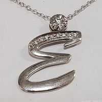Close-up of silver pendant shaped like letter 'E' with cubic zirconia stones and bezel set round cubic zirconia above it