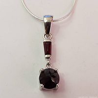 Close-up front view of the garnet pendant on silver chain showing the two garnet stones set in silver: a rectangular and a round garnet.