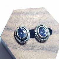 Close-up of pair of silver earrings with oval lolite stones in silver bezel setting on wooden display.