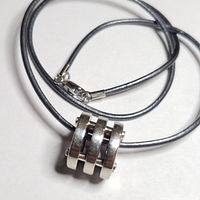 Photo showing a silver pendant shaped with three horizontal bands on a gray leather cord necklace with a silver clasp.
