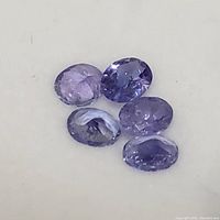 Close-up photo showing five oval faceted tanzanite gemstones laying on a white surface.
