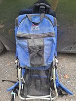 Front view of the blue Kelty Kids hiking backpack showing zippered front pocket and mesh cup holder, displaying signs of wear and water damage.