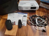 Multiple items on table: projector, case, remote, batteries, guides and cables