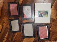 Top view of six black plastic picture frames on a wood floor, showing different sizes and some inserts.