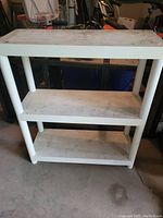 White plastic shelf unit with three levels, slightly dirty, displayed in a garage setting.