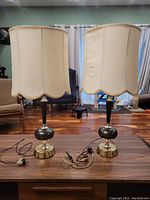 Front view of two vintage fabric shade lamps on wood table with cords visible.
