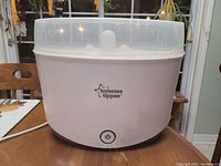 Front view of the Tommee Tippee baby bottle sanitizer showing the base unit with power button and clear lid on top, placed on wooden surface.