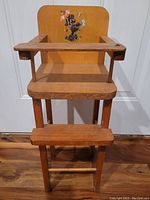 Full front view of vintage wooden doll high chair showing tray, seat, footrest, and backrest with poodle decal.