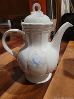 Side view of vintage porcelain tea or coffee pot showing blue floral pattern and curved spout and handle.