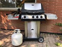 Full front view of grill on wheeled cart with one propane tank and utensils on side shelf