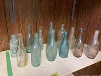 Row of thirteen assorted vintage glass bottles on wood shelf