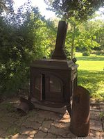 Full view of rusty outdoor Vigilant cast iron stove on a stone patio beside a rusty steel bucket with handle
