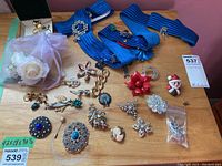 Overview of the collection showing blue belts, assorted brooch pins and small jewelry items on wooden surface