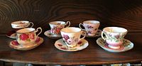 Six assorted bone china cups and matching saucers with various floral patterns and gold trim.