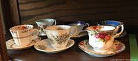 All six cups and saucers arranged in a single photo showing varied floral patterns and colors