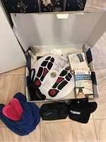 Photo of opened box showing Dr. Ho's circulation promoter device, blue fabric booties, black ankle straps, replacement pads box, user guides, and carrying pouch.