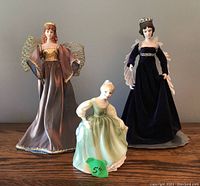 Photo of the Royal Doulton figurine and two tree topper angels arranged on a wooden surface against a gray background.