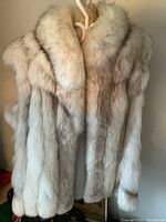 Front view of the Albert Ward sleeveless fur vest hanging on a hanger, showing the plush collar and full body of light colored fur.