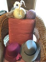 Hats and hat boxes displayed on a wicker chair with a rust-colored cushion, showing two hats and two round hat boxes.