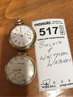 Two pocket watches side by side on a wooden surface with a note identifying them as Bulova and Waltham watches.