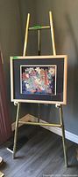 Full view of framed floral print displayed on gold metal easel in corner of room