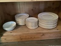 Wooden shelf displaying stacks of white china plates and bowls.