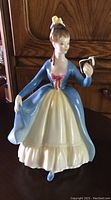 Front view of 'Leading Lady' Royal Doulton porcelain figurine with woman in blue bodice and yellow-cream skirt holding a book.