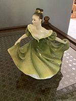 Front and side view of Royal Doulton figurine "Lynne" in green and yellow dress on glass table
