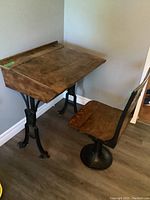 Side view of vintage school desk with wood top, inkwell hole visible, cast iron legs, and attached seat with cast iron pedestal base.