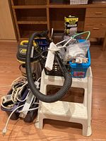 Overall view of lot arranged on and around white step stool showing Stanley shop vac, power strips, storage bins, cables, and Alien Tape box