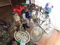 Top-down view of assorted art glass decor including crystal bells, suncatchers, plaques, and other ornamental pieces arranged on a glass table.