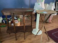 Two-tier wooden side table with curved edges and turned legs next to round wooden side tables with tripod legs, showing scratches and scuffs.