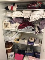 Shelves with multiple folded towels in white, purple, burgundy colors, storage baskets including wicker and metal, and framed wall art pieces.