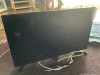 Front view of Samsung TV on stand with power cable and remote control in front.