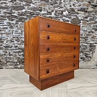 Three-quarter view showing front and right side, teak veneer finish, four drawers with recessed square pulls and plinth base.