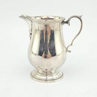 Front view of polished silver creamer on white background