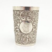 Front view of a sterling silver shot glass showing detailed floral and scroll engraving with British hallmarks and monogram.